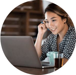 A smiling adult sat at a desk working on a laptop and speaking into a mobile phone.