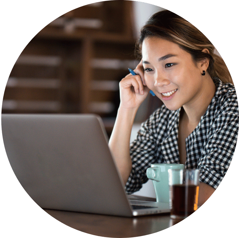 A smiling adult sat at a desk working on a laptop and speaking into a mobile phone.