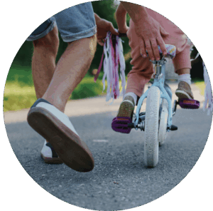 Adult pushing a small child on a bike . Only the legs and bike are seen in the picture.